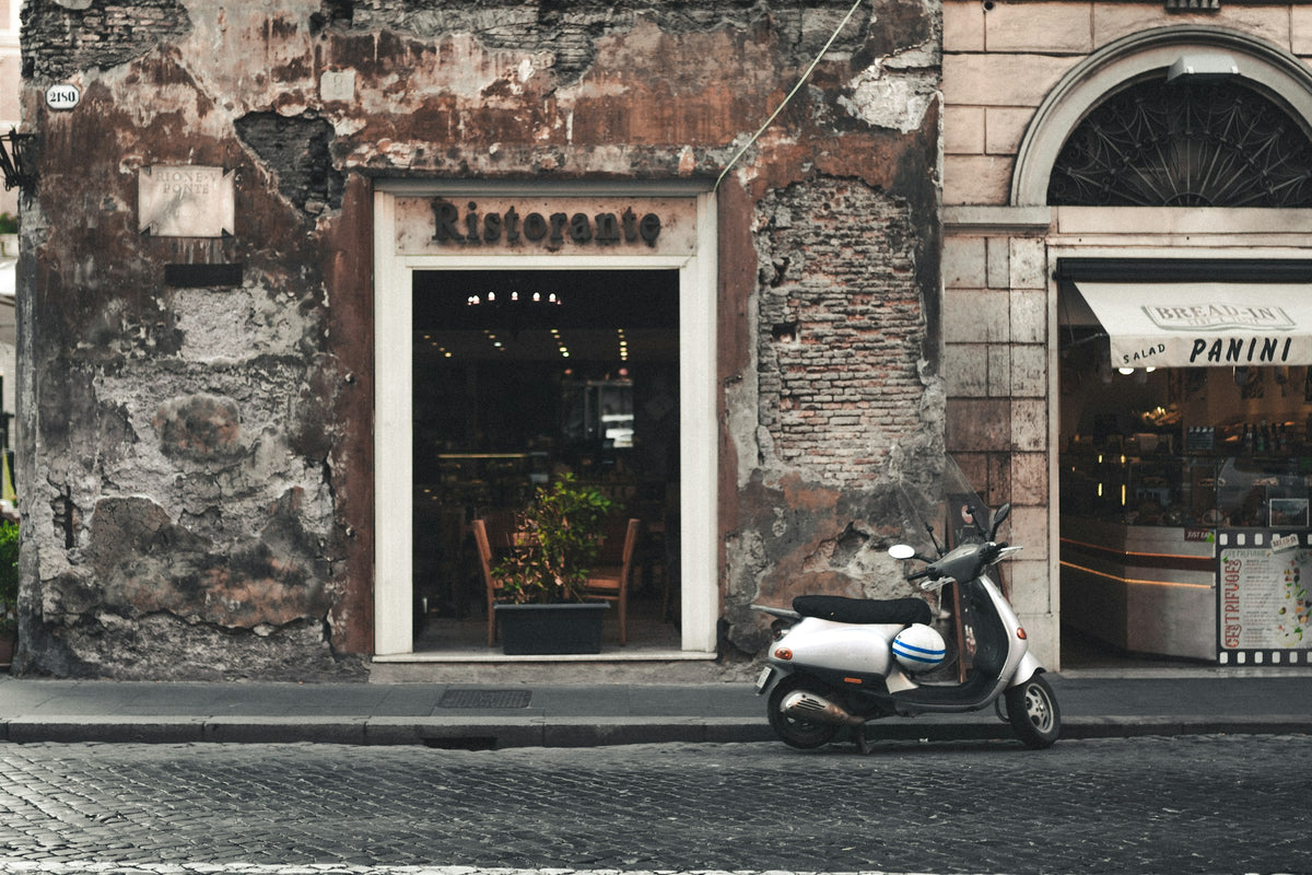 A scooter parked outside a ristorante with a weathered facade