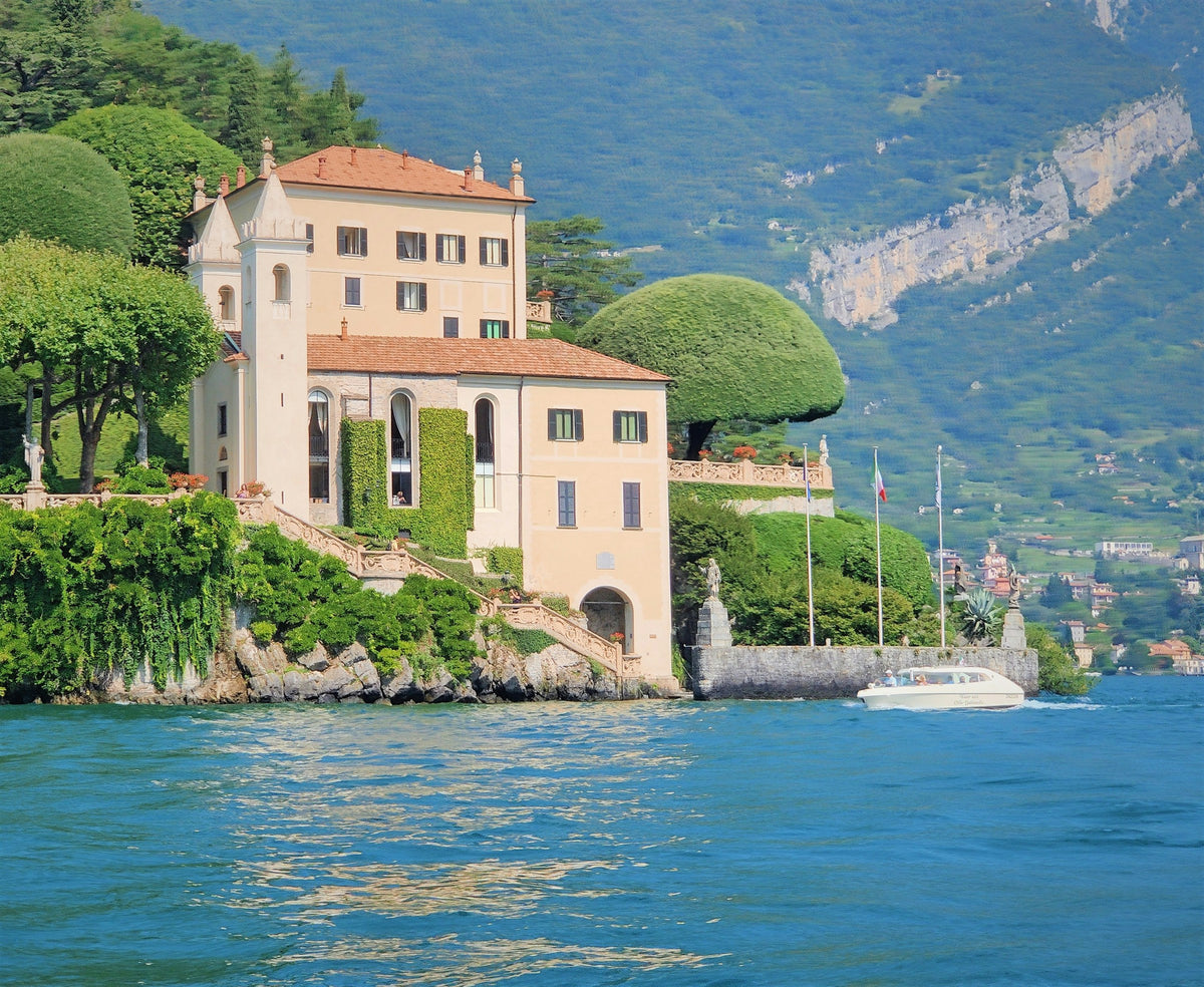 A white boat on the water below Villa del Balbianello