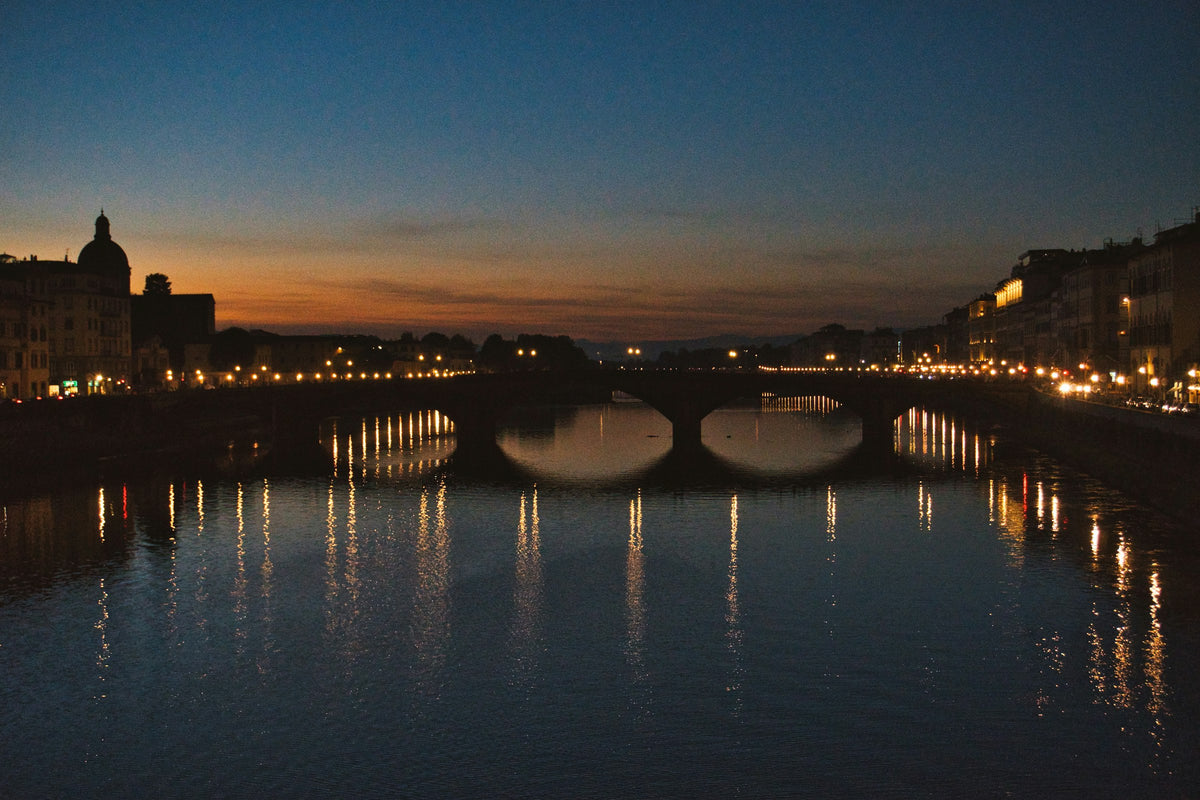 Lights reflected in the Arno beneath a bridge at dusk