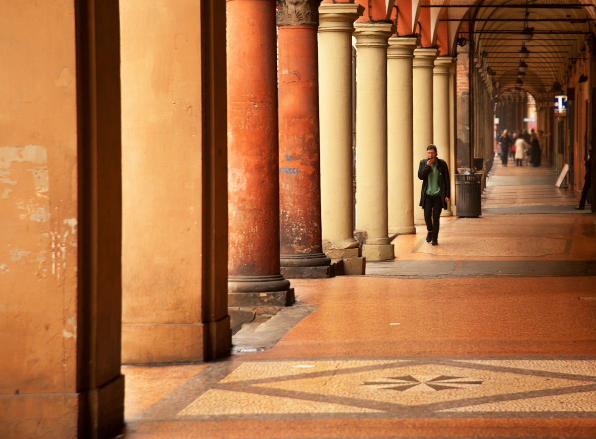 A man walking past the tall pillars of a Bologna portico