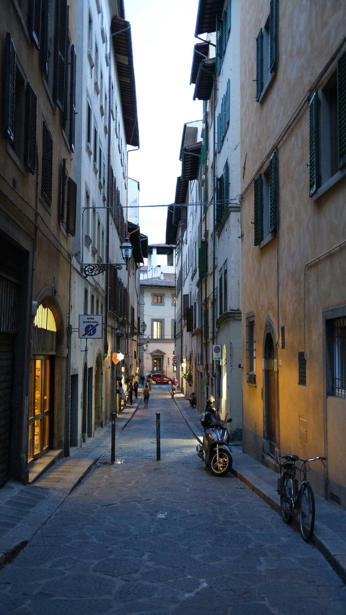 A scooter and bicycle in a long, narrow street of the centre