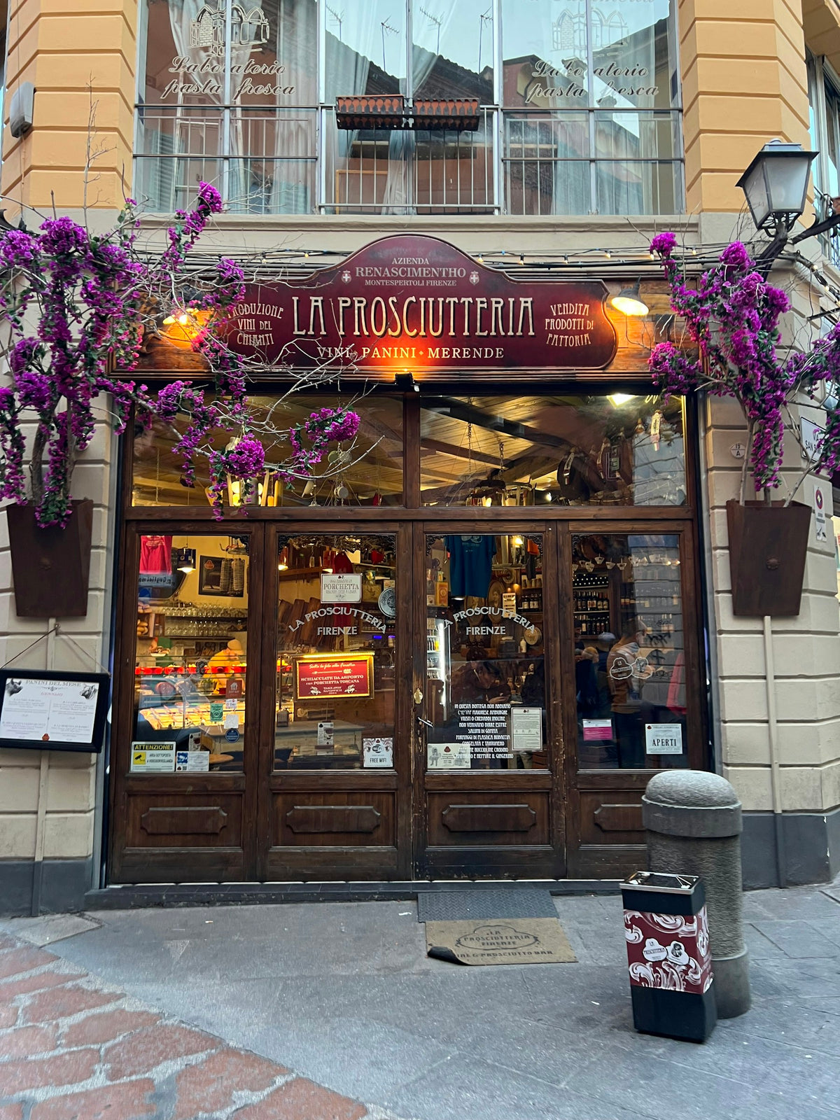 The storefront of a prosciutteria in Bologna, with flowers hanging above
