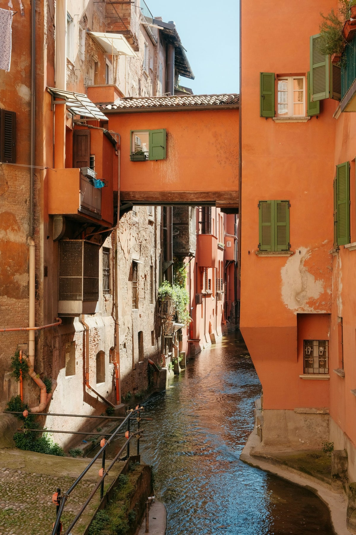 A canal flowing between houses with green shutters in Bologna