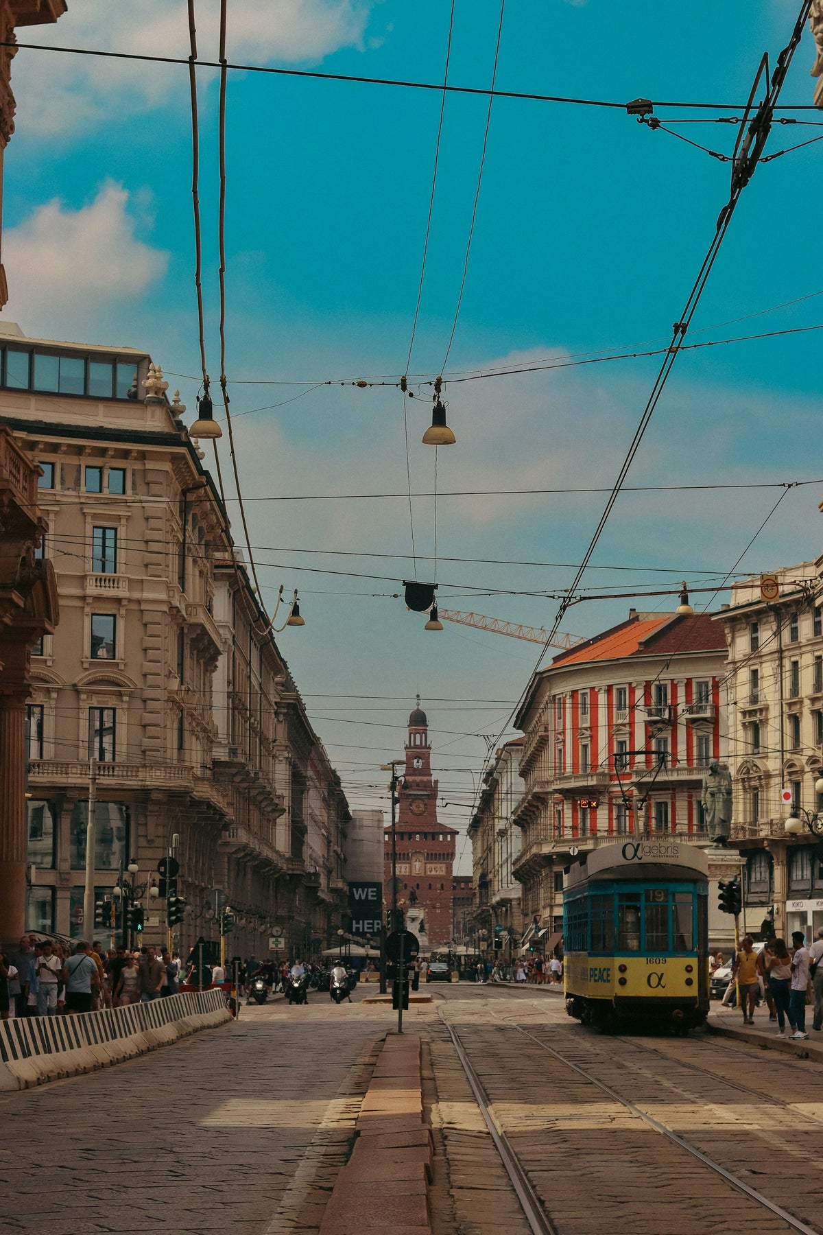 A yellow tram on a Milan street, with the Castello Sforzesco tower in the distance