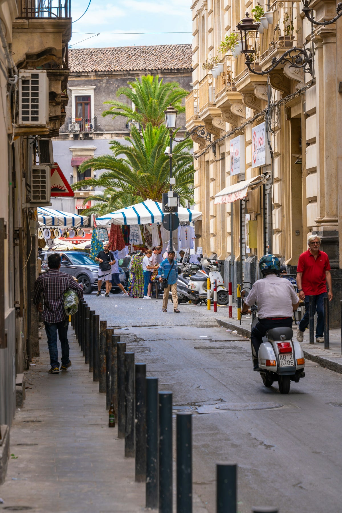 A weekday street with scooters and market stalls