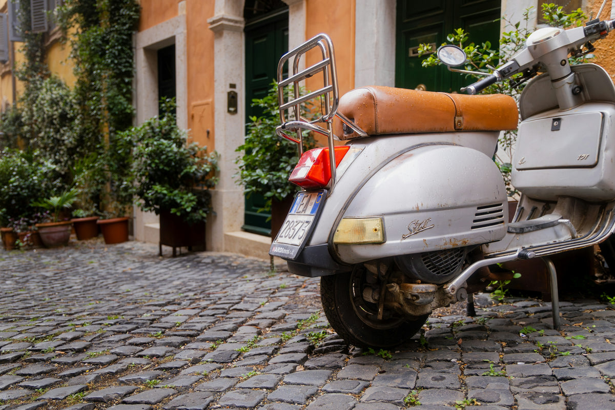 A Vespa parked on the cobbles beneath potted plants