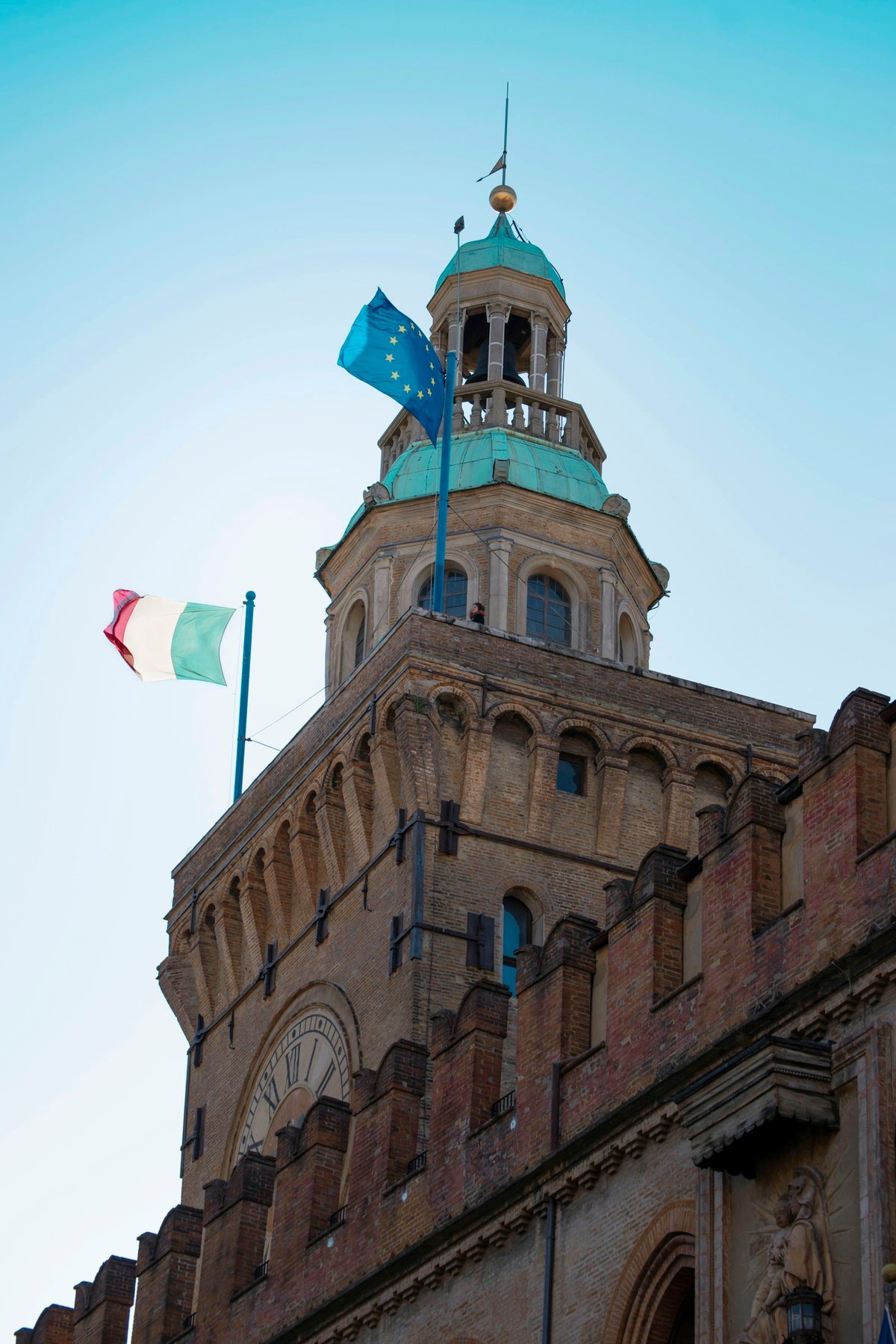 A historic building in Bologna with flags against a blue sky