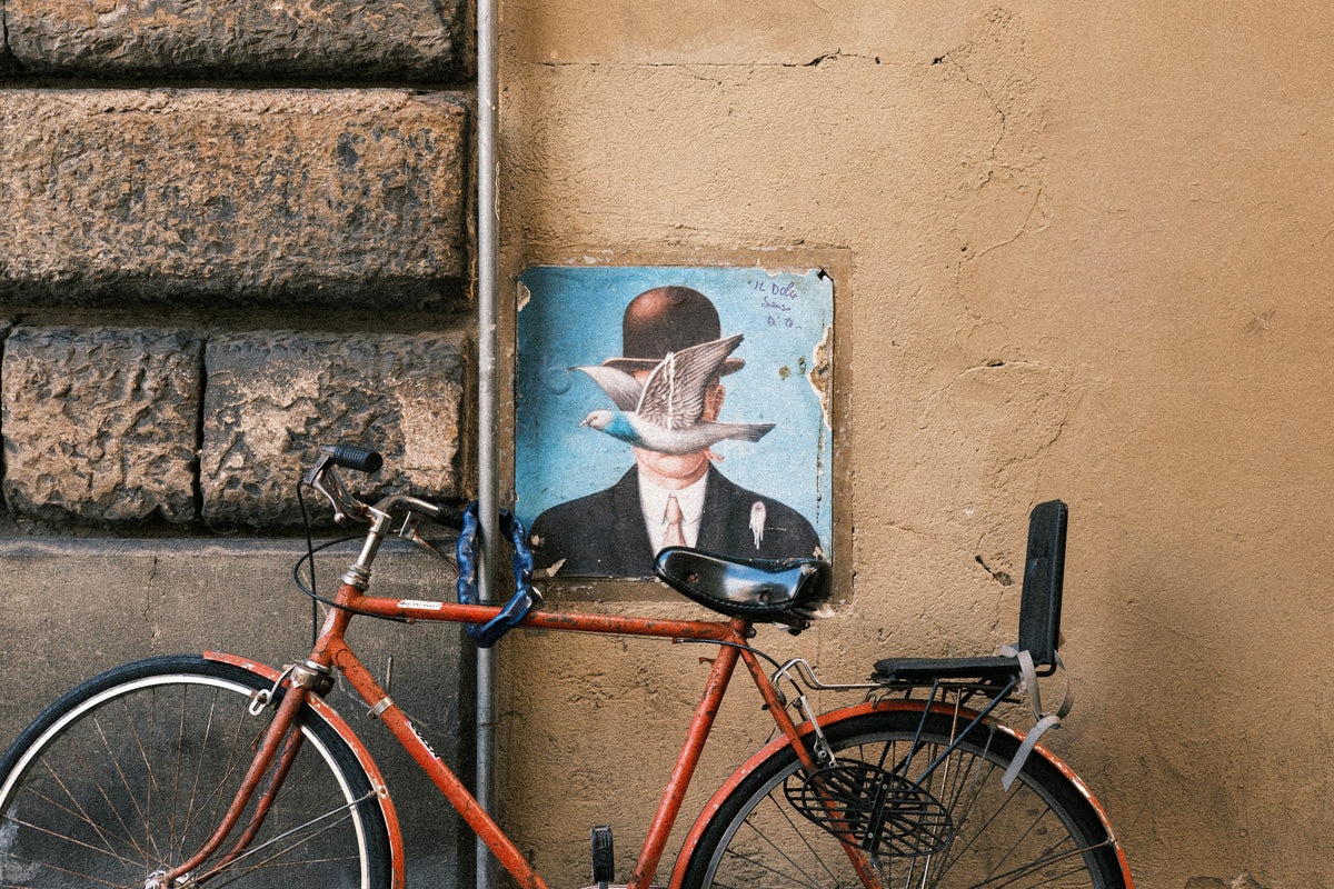 A red bicycle beside a street-art poster on a Florentine wall