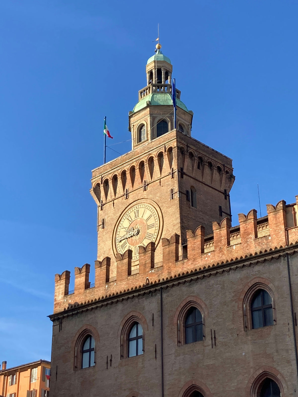 A crenellated clock tower in Bologna against a blue sky