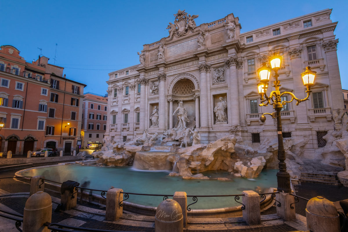 The Trevi Fountain at dusk, with the street lamps lit