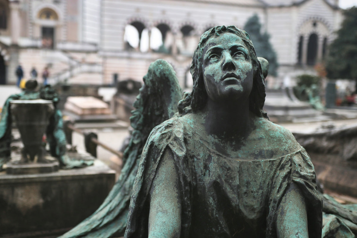 A weathered bronze angel sculpture in a Milan cemetery