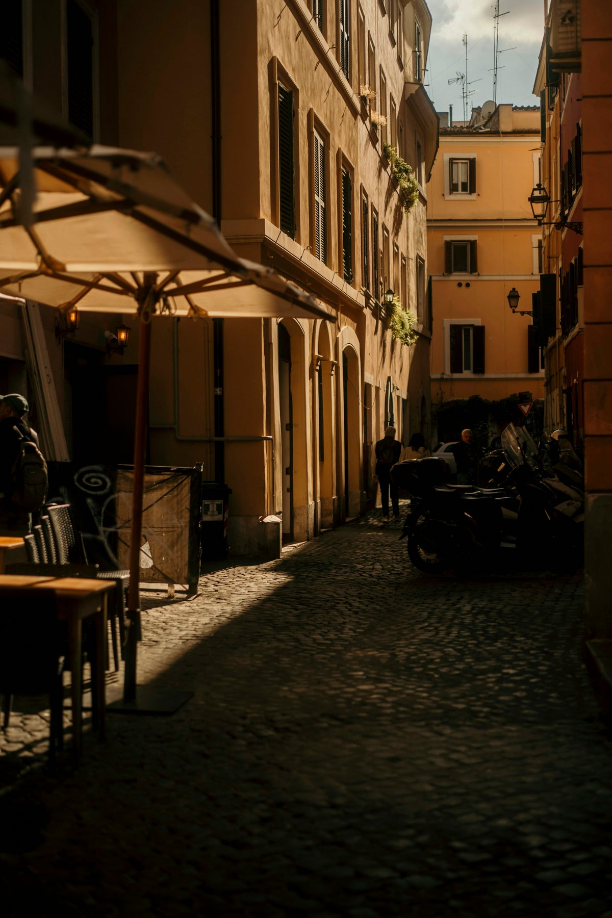 Café tables in the shade of a narrow street in the late afternoon