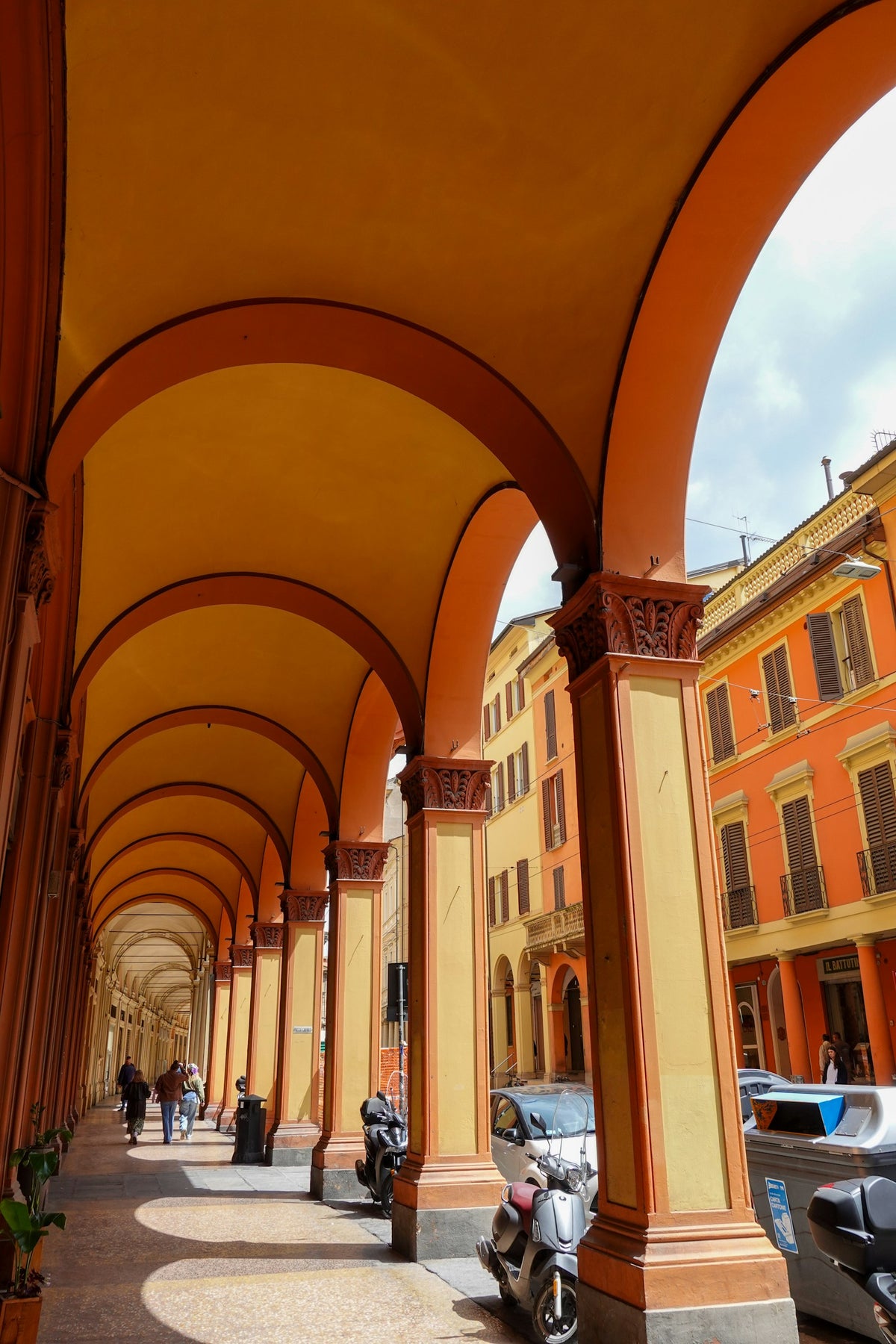 People walking under a historic orange and yellow portico