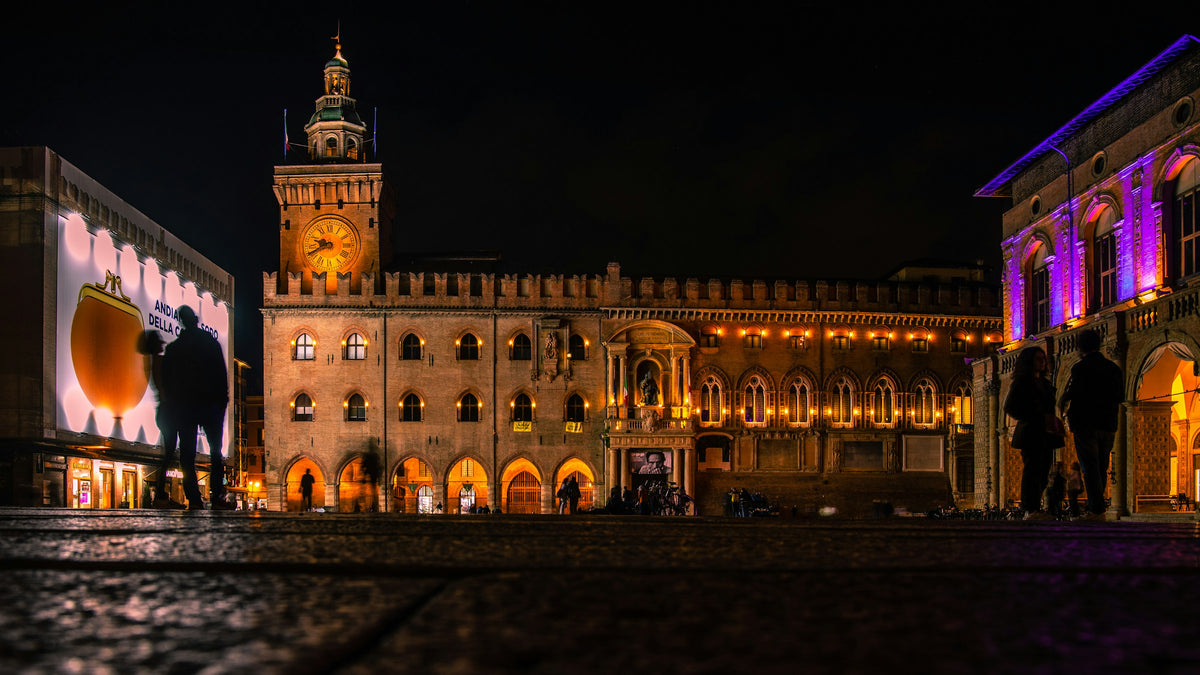 Piazza Maggiore at night, with the illuminated Palazzo d'Accursio and people in the square