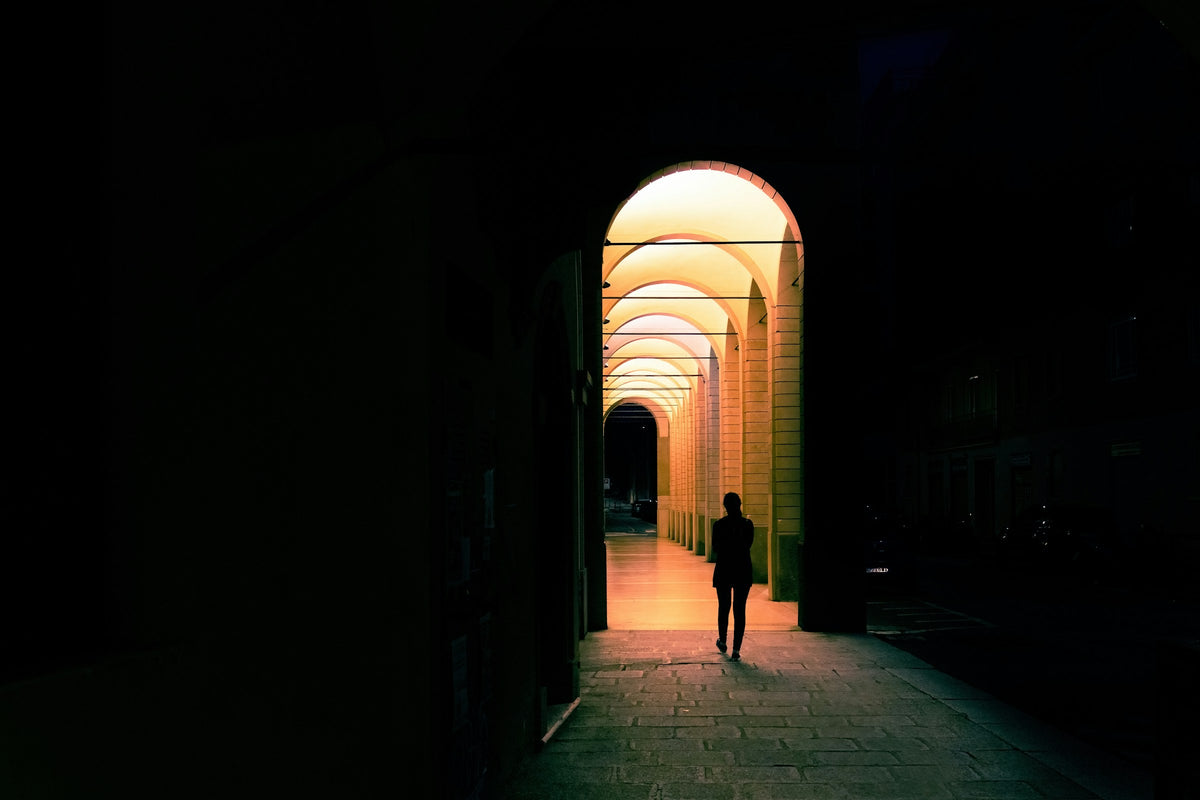 A lone pedestrian under warmly lit arches on a Bologna street at night