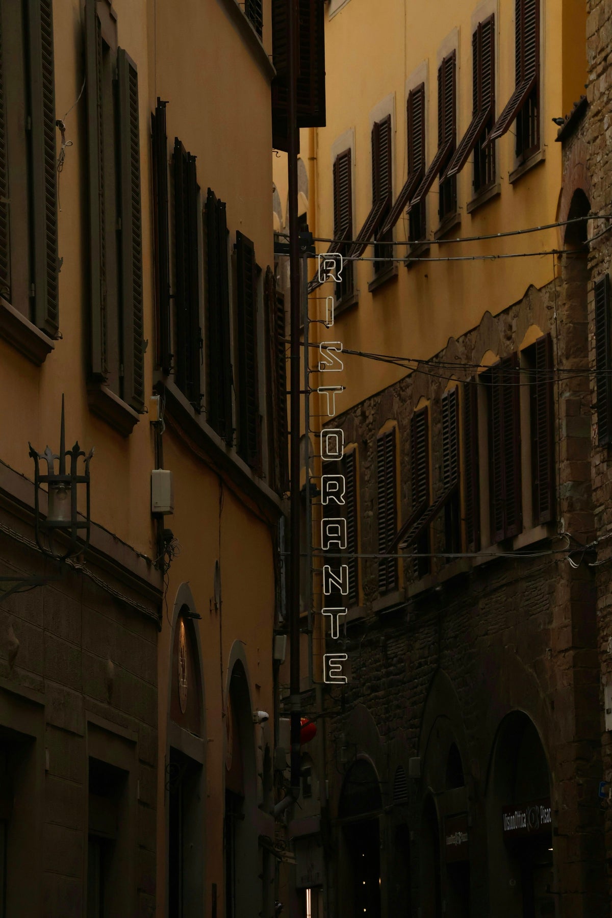 A vertical neon ristorante sign glowing in a narrow lane