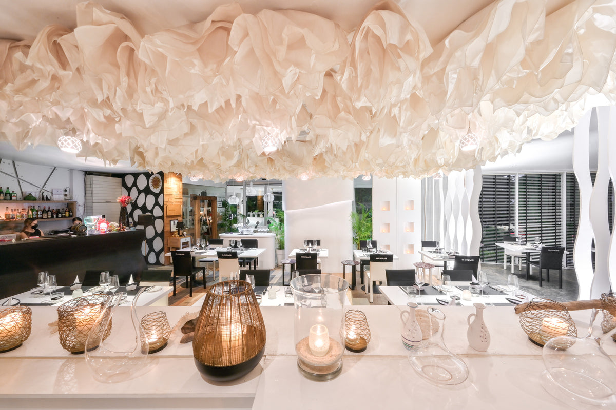 White dining room with sculptural cloud-like ceiling and candlelit tables at Acqua Restaurant