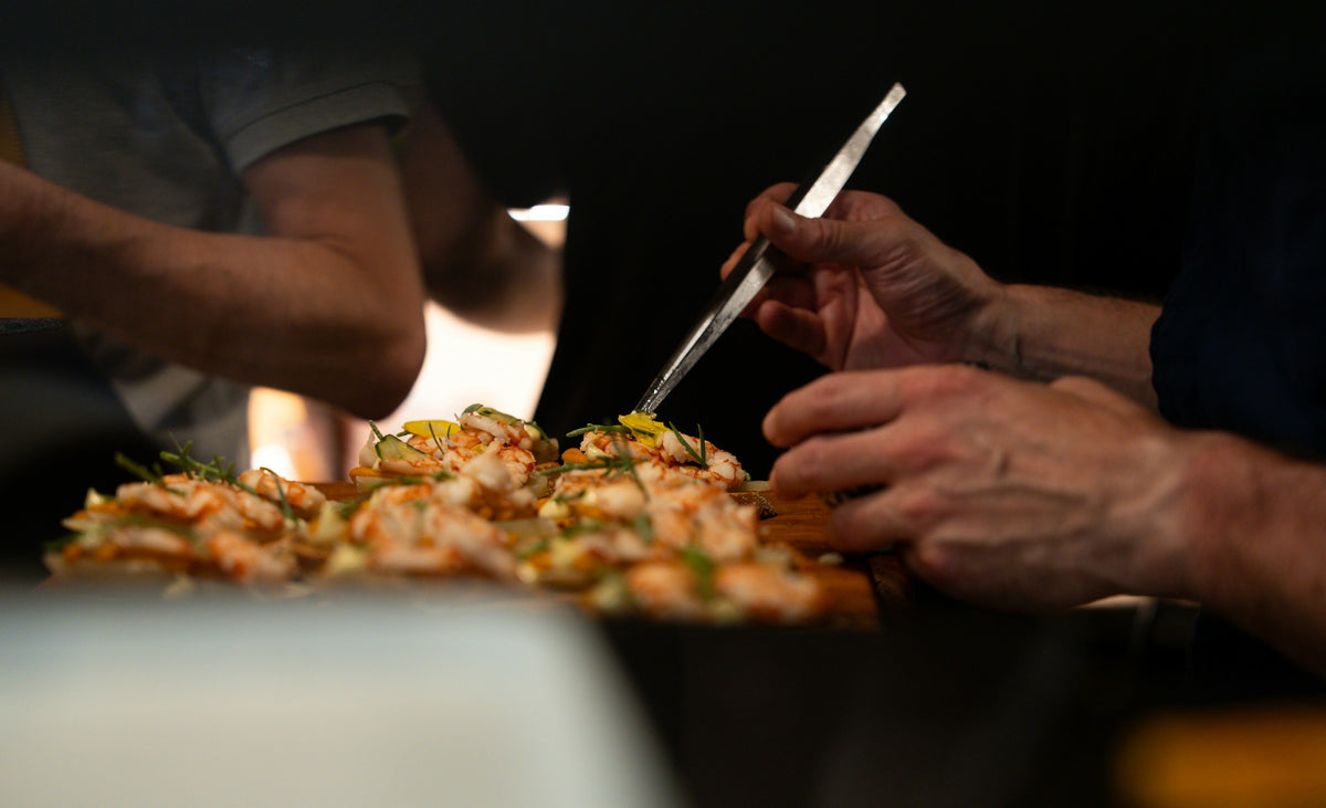 Hands garnishing a tray of prawn crostini