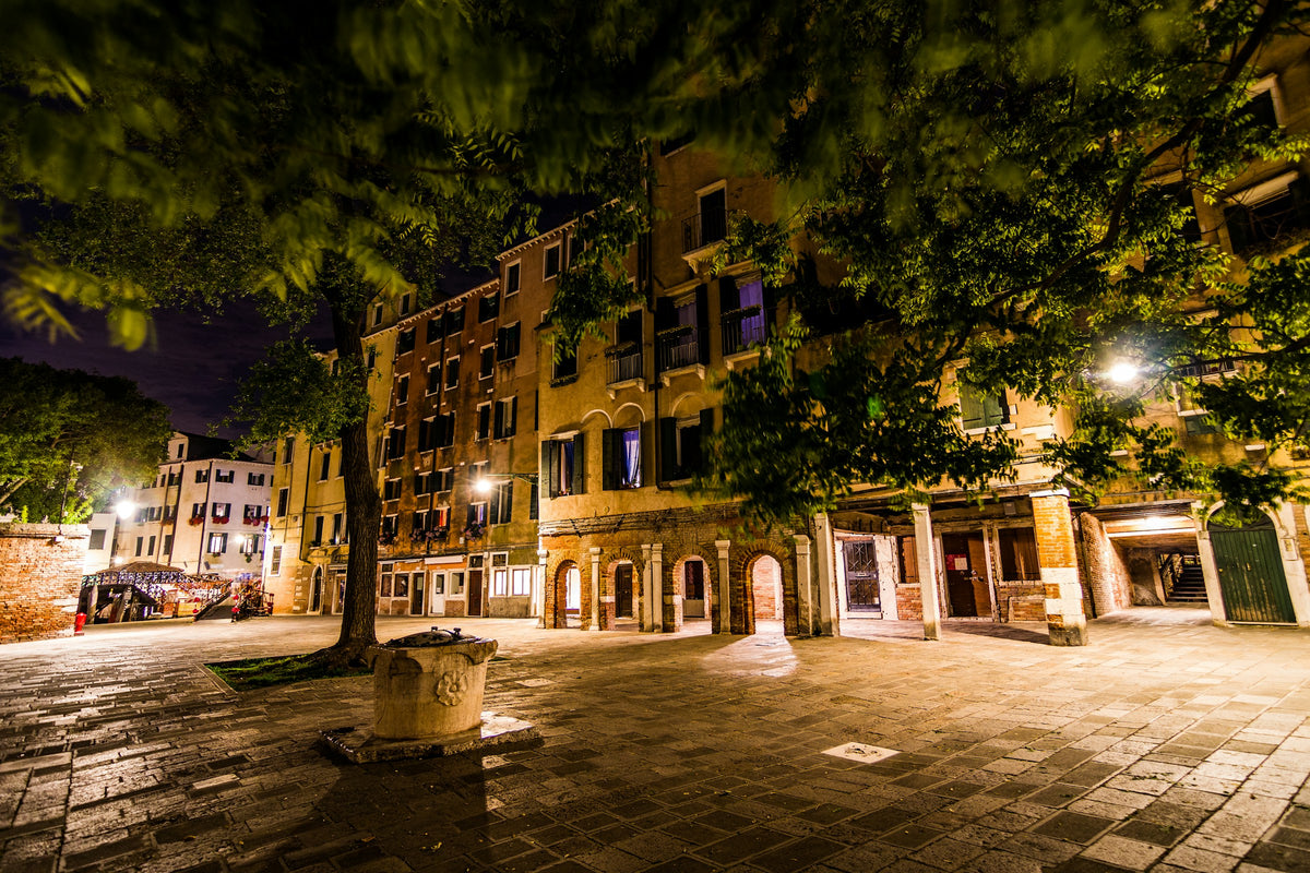 A campo in the Venetian Ghetto at night, with trees and an old wellhead