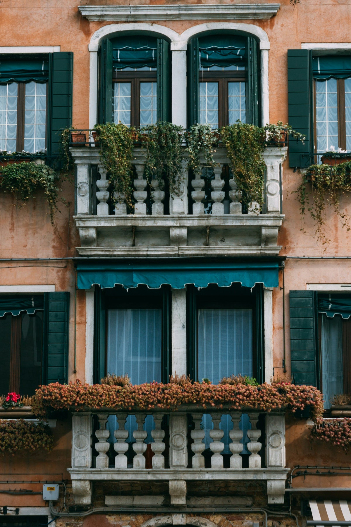 Flower-filled balconies and green shutters on a Venetian facade