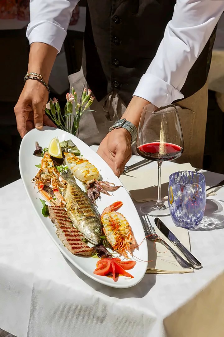 Grilled fish and prawn platter served at a table with red wine