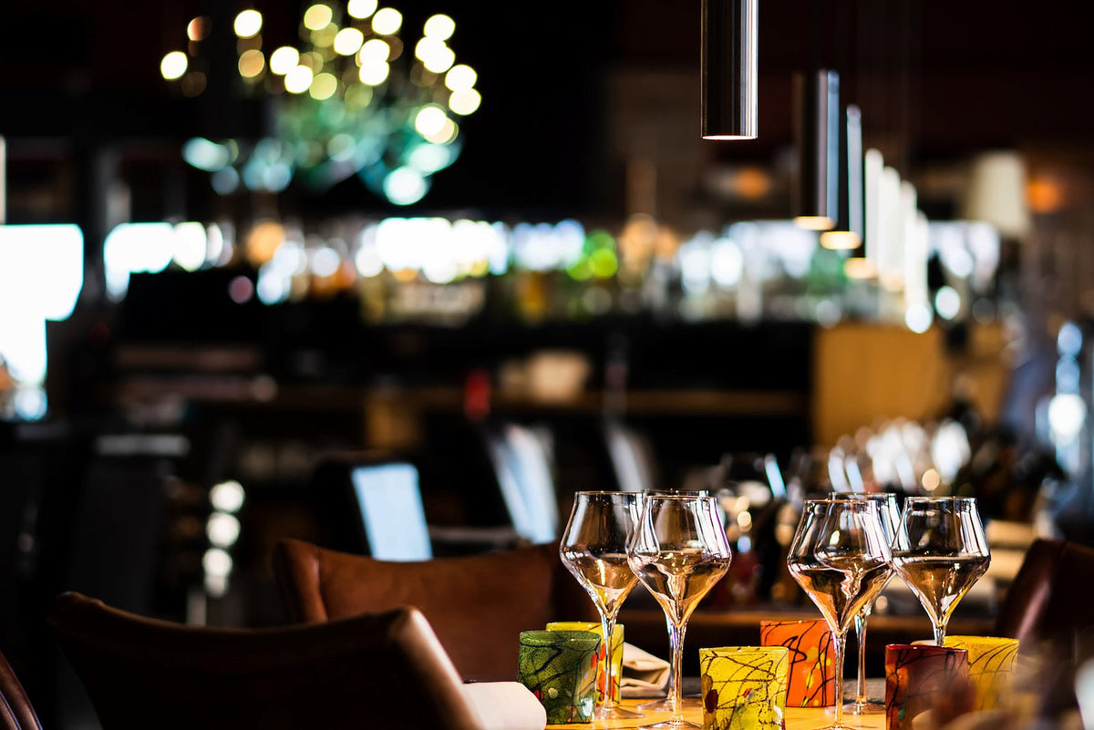 Wine glasses and colourful tumblers on a table under glowing chandeliers