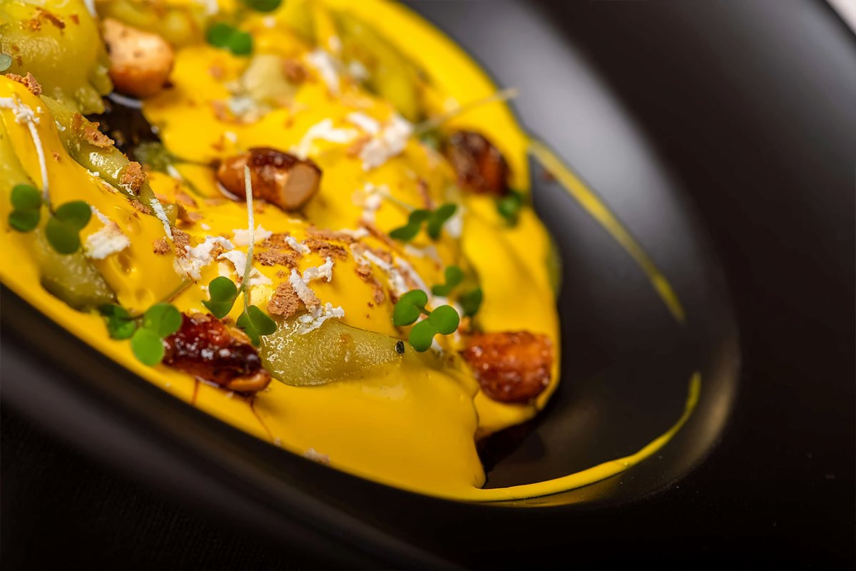 Filled pasta in a bright yellow sauce with seared toppings and microgreens