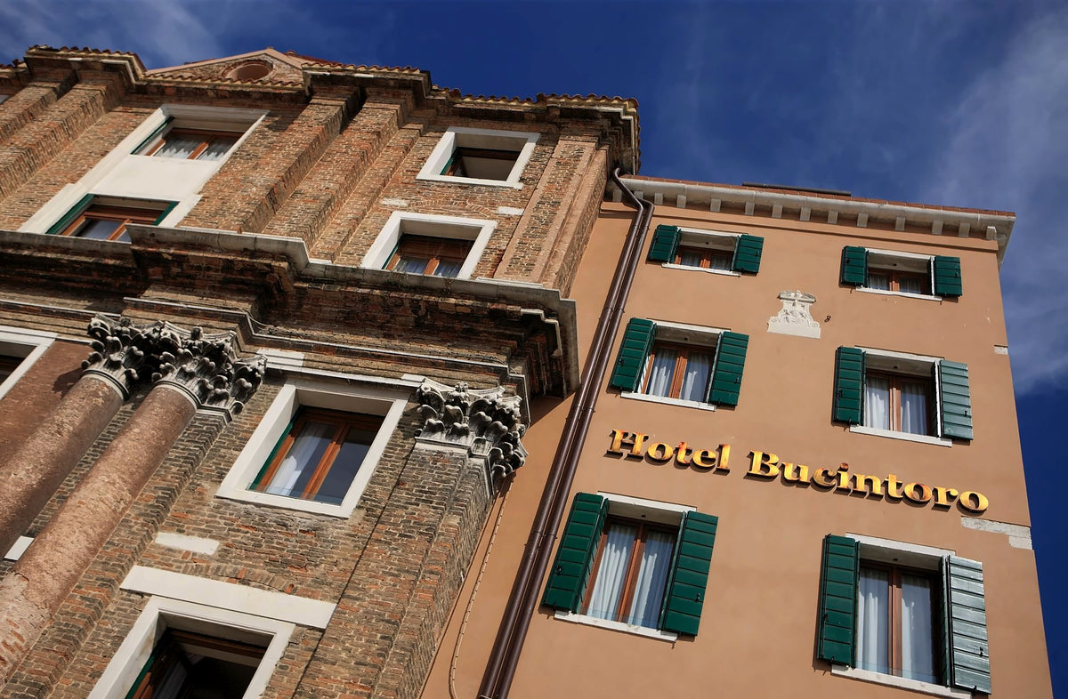 Hotel Bucintoro facade with green shutters beside a historic brick church front