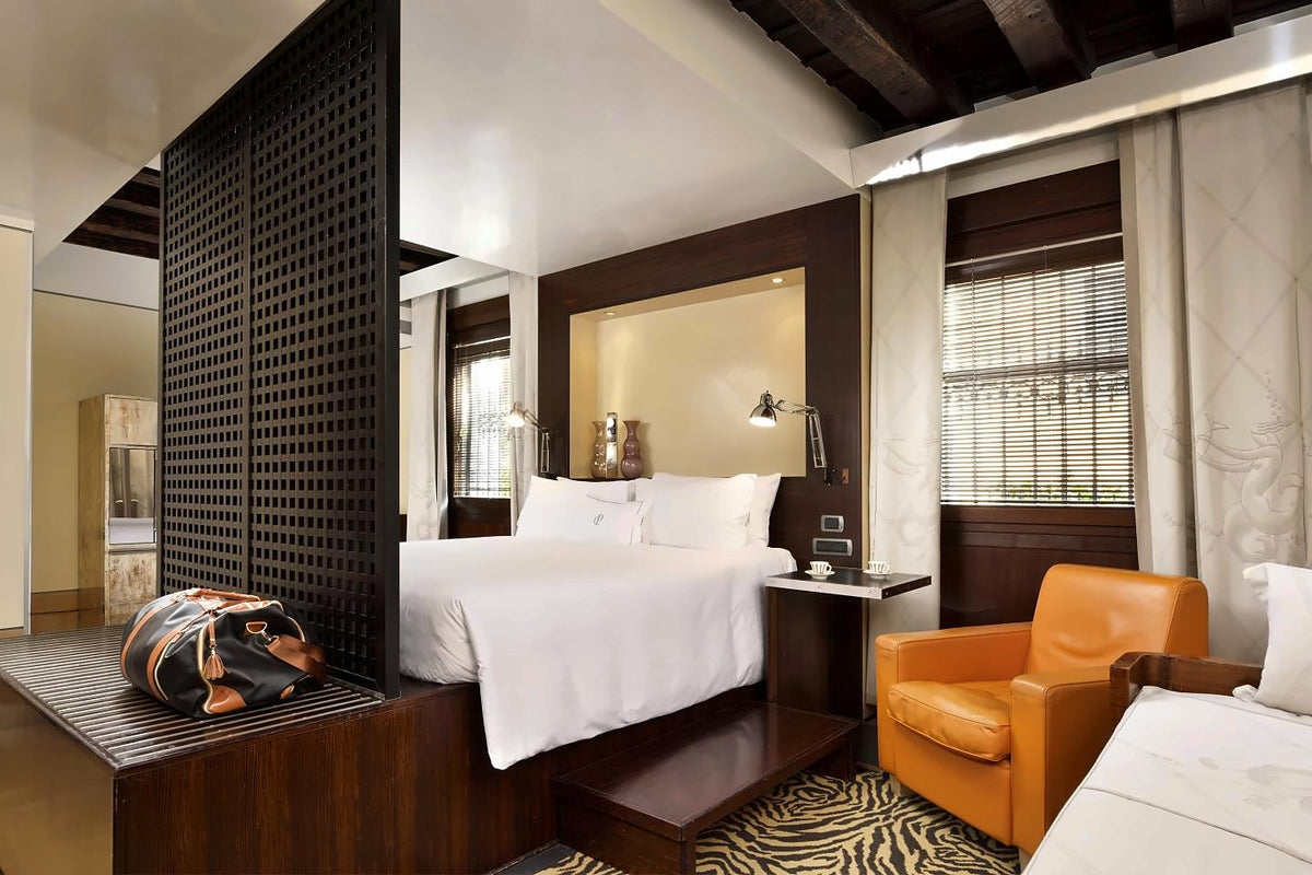Design room with dark wood screen, double bed, orange armchair and beamed ceiling
