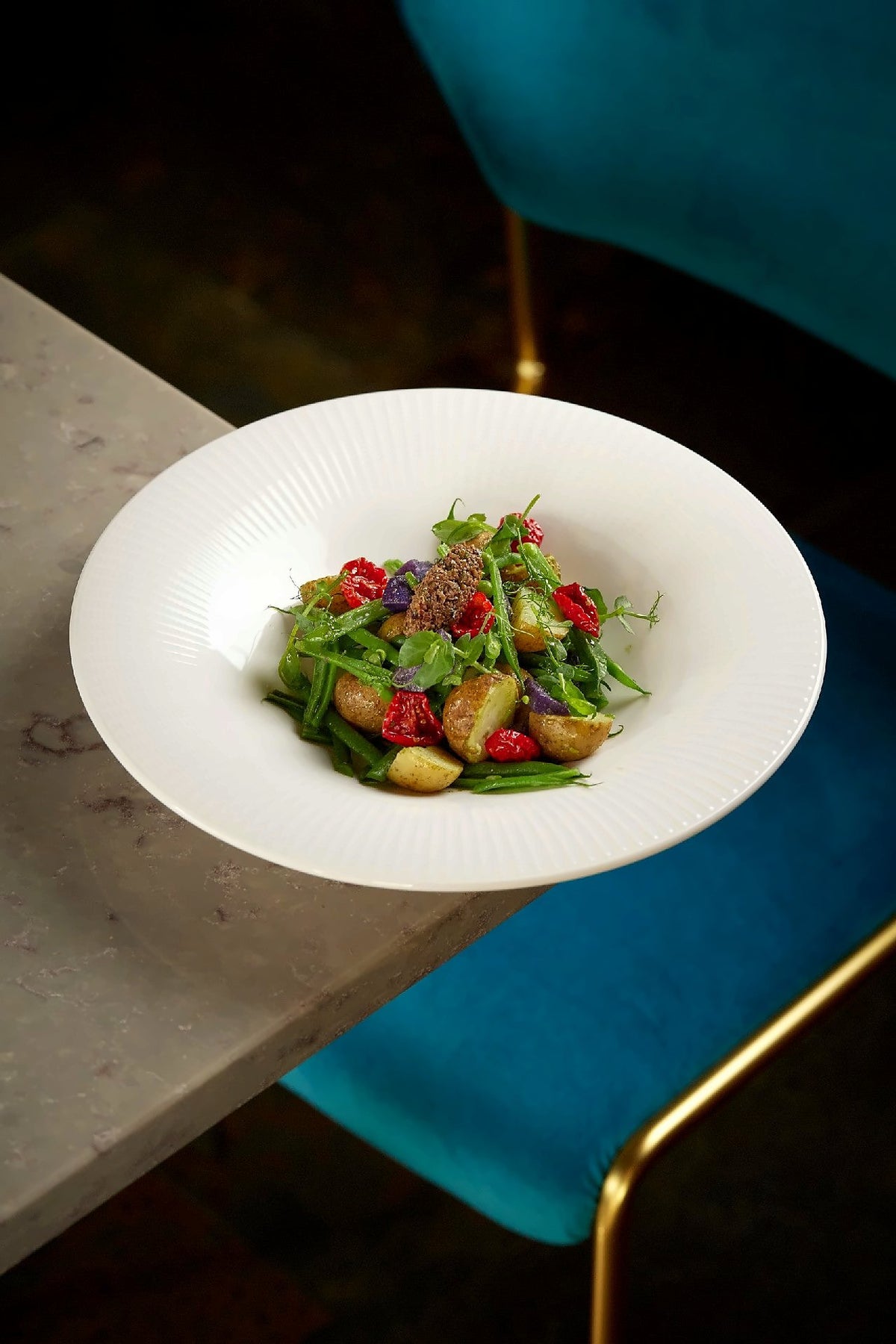 Green salad with potatoes and cherry tomatoes beside a velvet chair