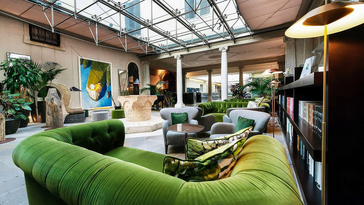 Glass-roofed winter garden lounge with green velvet sofas, plants and books