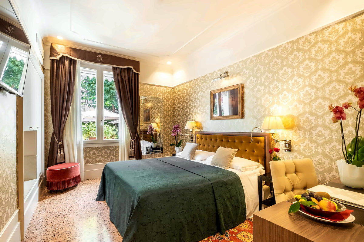 Room with green bedspread, damask wallpaper and windows onto greenery