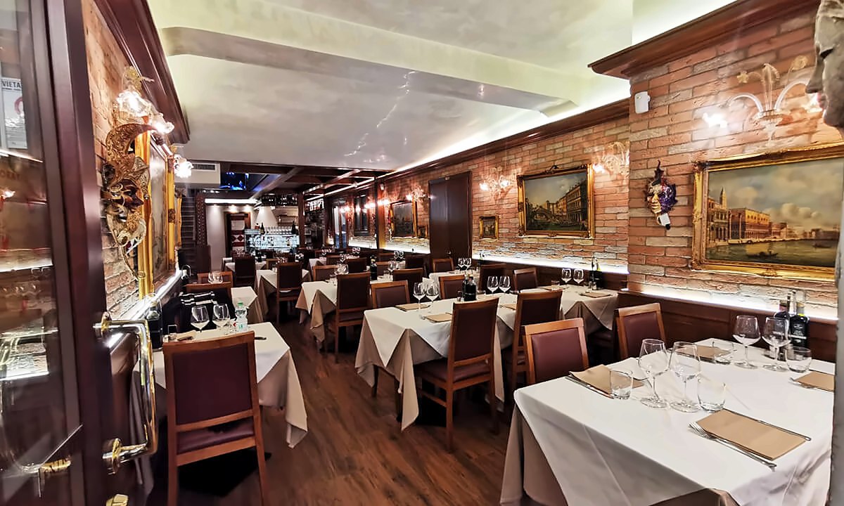 Long dining room with paintings and white tablecloths at Ristorante La Piazza
