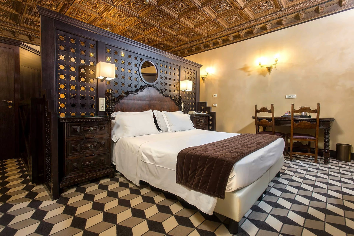 Room with carved wooden headboard, coffered ceiling and geometric tiled floor
